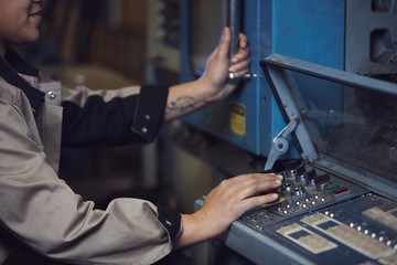Closeup of unrecognizable female worker turning handles while operating machines at production factory, copy space