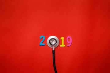 Naklejka premium Wooden colorful on text 2019 banner for health care and medical concept. black stethoscope,on table red background.