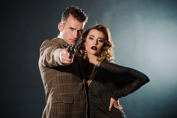 selective focus of dangerous gangster holding gun and standing near attractive woman  on black