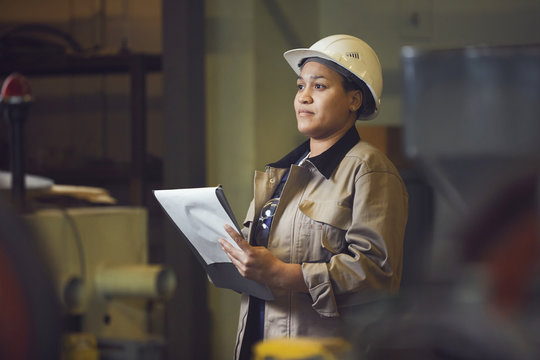 Waist up portrait of female foreman holding clipboard while supervising production at factory, copy space