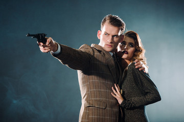 selective focus of dangerous man holding black gun near woman on grey