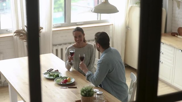Happy couple talking clinking glasses sit at table at home