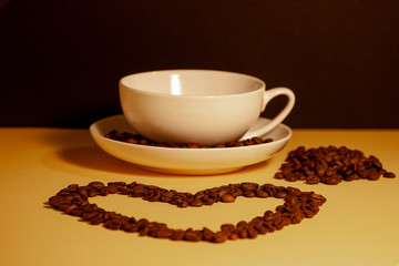 Heart shape made from coffee beans in front of a cup of coffee