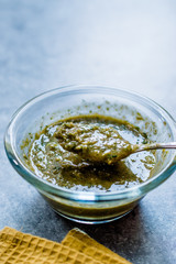 Homemade Green Herbal Salad Sauce with Plant Roots in Glass Bowl with Spoon.