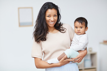 Portrait of beautiful young mother standing and holding her cute baby boy on her hands and smiling at camera