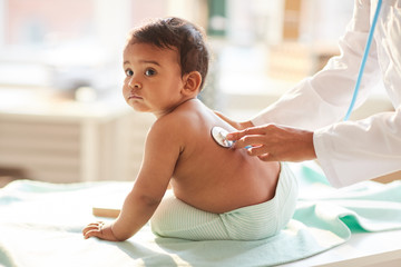 Cute toddler sitting on the table while pediatrician listening to his heartbeat at hospital
