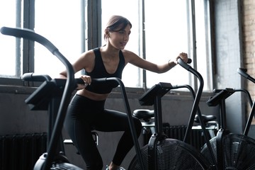 Fit young woman using exercise bike at the gym. Fitness female using air bike for cardio workout at gym