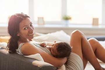 Side view portrait of young African-American mother breastfeeding cute baby boy and looking at...
