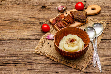 Homemade Thanksgiving garlic mashed potatoes with fresh tomatoes and pastrami. Sackcloth napkin, spoons, old wooden boards background