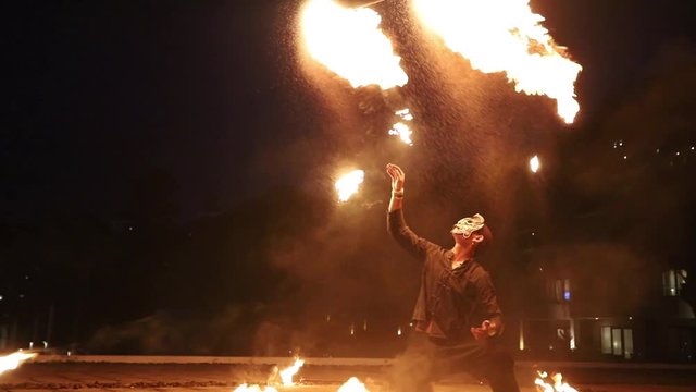 Man in black suit with thai style, wearing mask and barefoot performing fire club show on the hotel roof at night, throw the flame club up in the air two time slow motion
