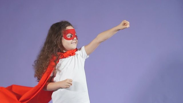 Positive little girl enthusiastically raised arms up, dressed in red mask and red cloak. Spaceman concept