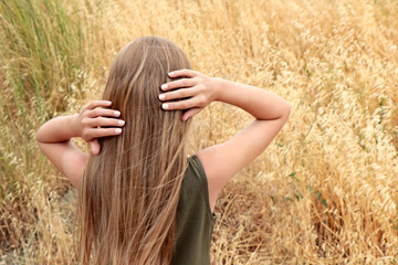 Little beautiful girl with blond hair and manicure on nails with light milk nail polish in the summer in the field.