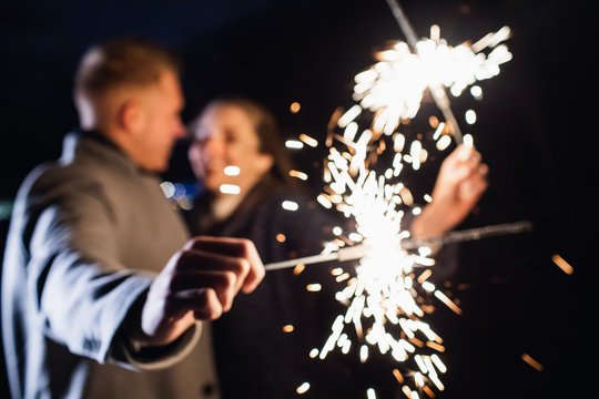 Selective focus of sparklers in hands of young couple enjoying holiday time outdoors