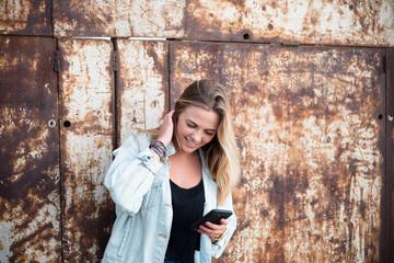 one beautiful blonde woman using her phone in the street - happy teenager alone on the road surfing in the social networks