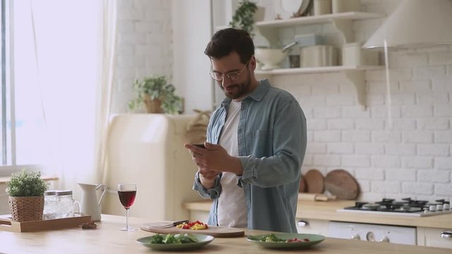 Happy young man preparing romantic dinner using smartphone mobile apps