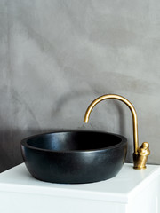 Black sink, vintage copper faucet, gray concrete surface wall, round mirror, loft bathroom interior...
