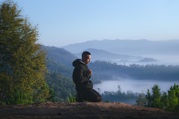 Fototapeta na wymiar Man sitting and praying on mountain in morning. Christian pray concept.