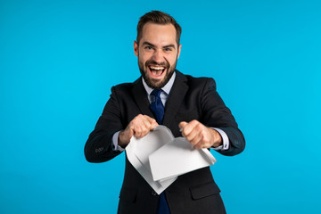 Serious businessman tearing contract in pieces. Angry furious male office worker throwing crumpled paper, having nervous breakdown at work, screaming in anger, stress management. 