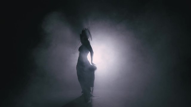 Silhouette dancer woman performing dance figures in fog. 4K Slow motion footage.