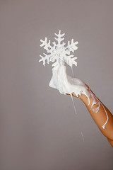 White painted hand holding a white colored snowflake melting down