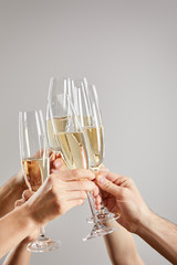 cropped view of women and men toasting while holding champagne glasses with sparkling wine isolated on grey