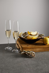 oysters and fresh lemons in bowl near champagne glasses with sparkling wine isolated on grey