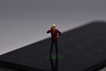 miniature man standing on a phone talking with a smartphone