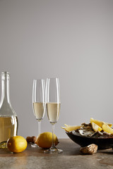 champagne glasses with sparkling wine near bottle, oysters and lemons in bowl isolated on grey