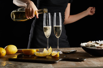 cropped view of woman pouring sparkling wine in champagne glass near oysters in bowl with ice isolated on black