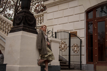 Fashion european woman walking at the street, dressed modern clothes. Female moder wearing faux fur coat, tutleneck, skirt, and curl hairstyle