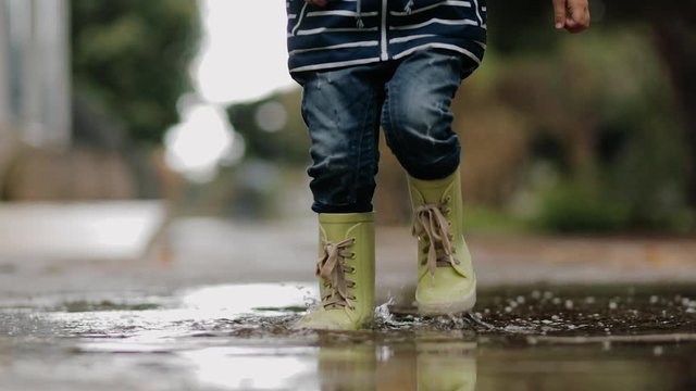 Little boy walks through puddles in rubber boots during the rain