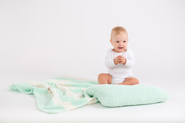 Kid boy sitting on the plush striped double colored blanket on the white background