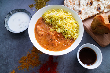 Butter chicken with curry rice, samosas and Naan bread on concrete background. Indian cuisine. Top view.