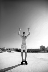 Young attractive man posing in front of camera on the roof of a residential building. Hands up in the air