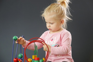 Toddler girl playing with wire bead maze toy. This colorful educational wooden toy teaches children hand-eye coordination, motor skills and colors.