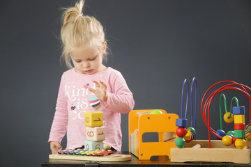 Adorable blonde toddler girl playing with her toys, studio portrait against dark backgraund