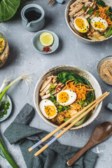 Asian style ramen noodle soup with bok choy, carrot, lime, sesame seeds, chicken and egg, gray background