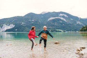 A senior pensioner couple hikers standing barefoot in lake in nature. - Powered by Adobe