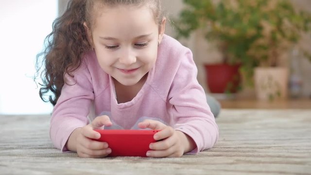 Cute baby entertaining with a mobile phone or tablet. Little girl spends her free time playing a mobile game and crushes a bright screen with her hand. Concept: Happy Childhood, Games for children.