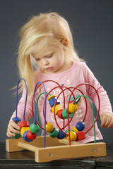 Fototapeta na wymiar Toddler girl playing with wire bead maze toy. This colorful educational wooden toy teaches children hand-eye coordination, motor skills and colors.