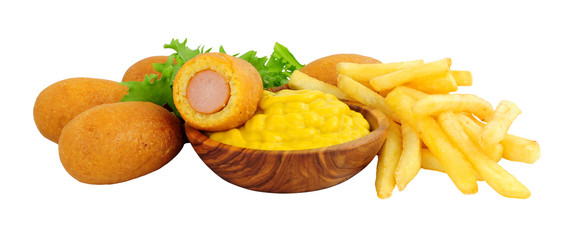 Mini party corn dogs on wooden sticks and French fries with a wooden bowl of American mustard isolated on a white background