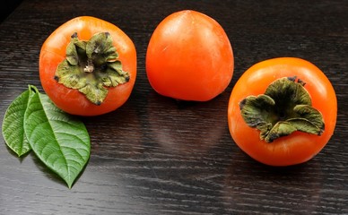 Ripe persimmon fruits are on a dark wooden table