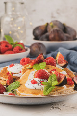 Pancakes with raspberries, figs, yogurt, coconut zest, honey and mint leaves on a plate.