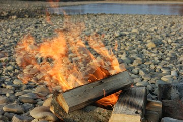 Bonfire burns on pebbles of a river bank, background
