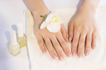 Obraz na płótnie Canvas Beautiful soft woman hands with light manicure hand care and spa relaxing white orchid nail polish towel copy space