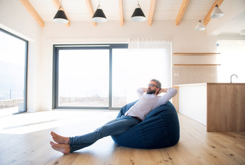 Happy mature man moving in new unfurnished house, sitting on bean bag.