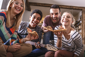 Group portrait of friends making fun at the home party.They sitting in living room and eating pizza.