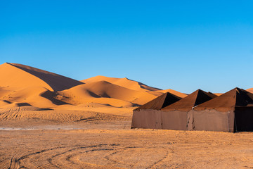 Fototapeta na wymiar Luxury brown tent camp in Sahara Desert Merzouga, Morocco on a sunny day with sand dunes on background