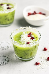 Party Christmas healthy vegetarian dessert, kiwi smoothie sprinked with coconut flakes and pomegranate seeds. Selective focus, space for text.