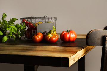 Tomates variedad sobre tabla rústica y cesta de metal con tomates naturales frescos y planta de albahaca sobre mesa de madera rústica. Vista de frente